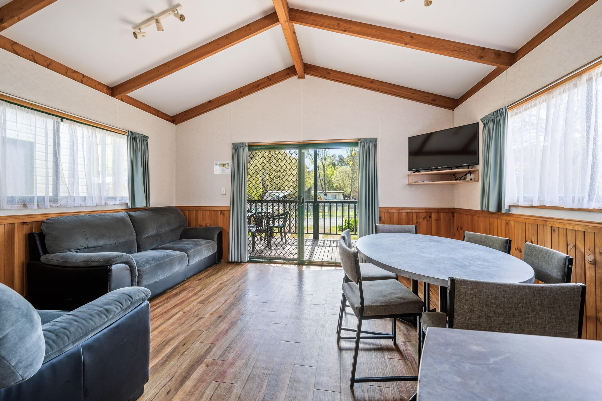 Spacious Supreme Villa living area with timber beams, leather lounges, dining table and private deck at Bright Accommodation Park