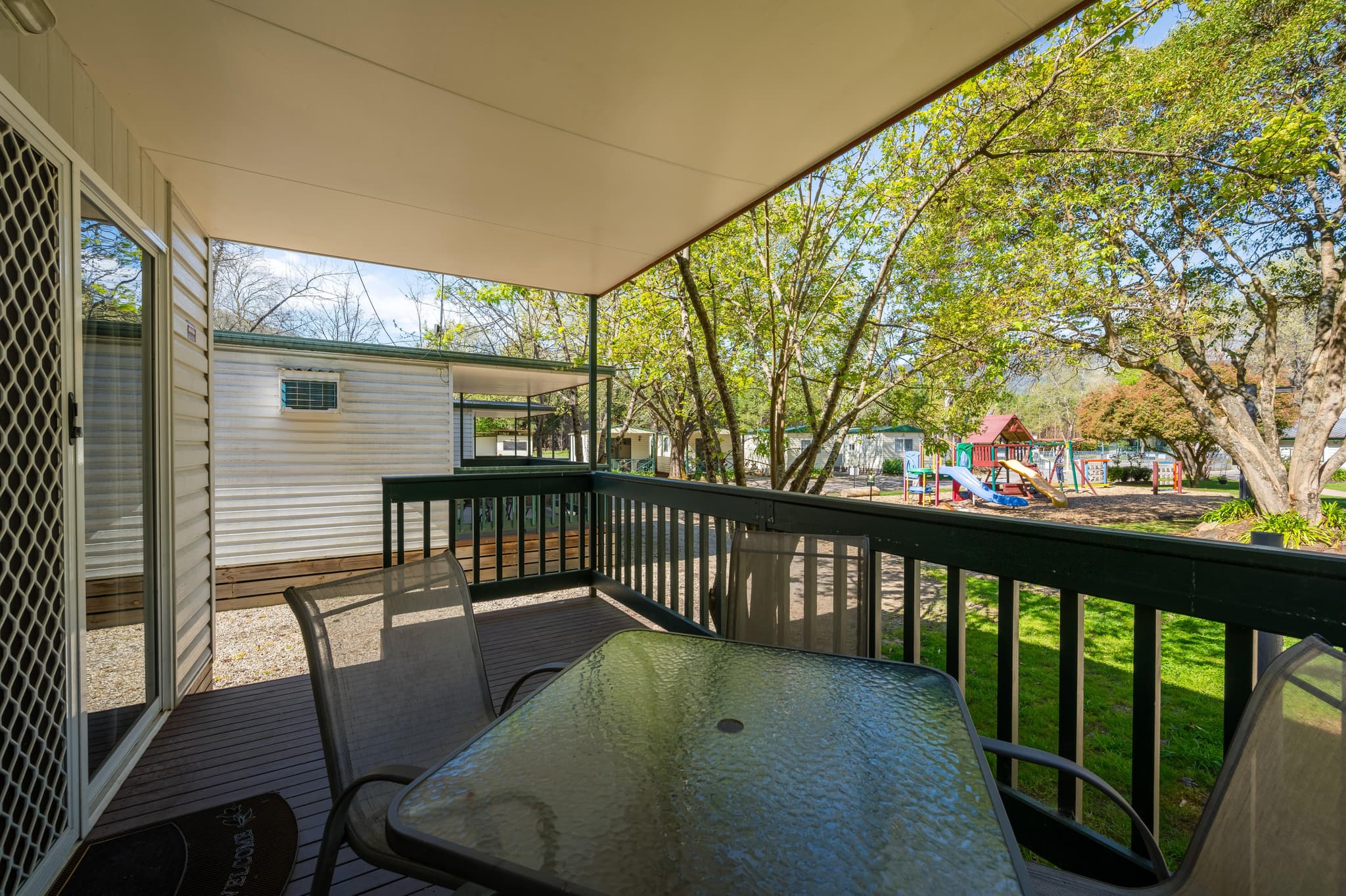 Private deck with outdoor dining at Bogong Cabins, Bright Accommodation Park, overlooking children's playground and gardens