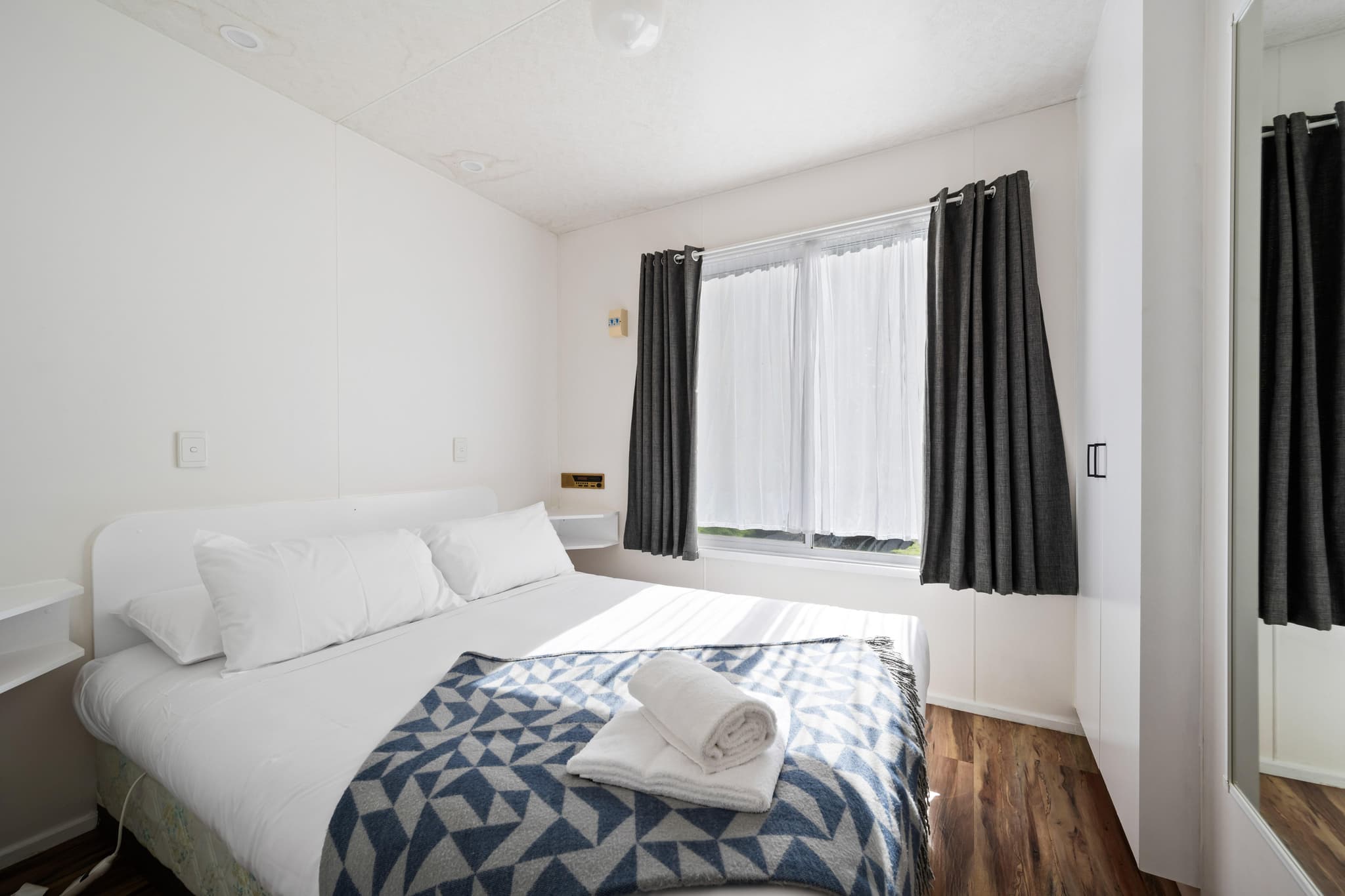 Clean modern bedroom in Bogong Cabins at Bright Accommodation Park with queen bed, white linen and dark curtains