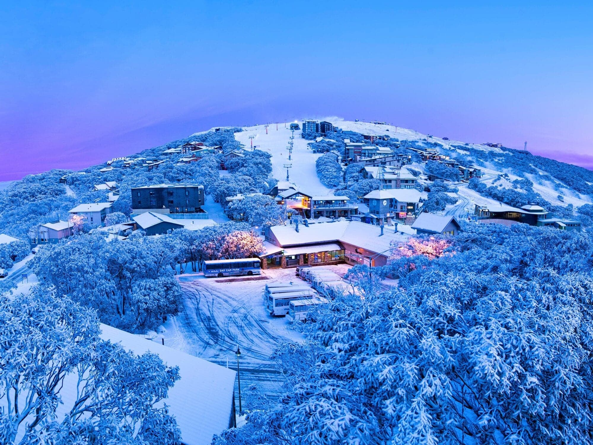 Snow-covered Mt Buller ski village at dusk, near Bright Accommodation Park, with chairlifts and frosted snow gum